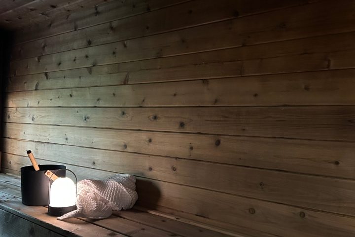 Wooden sauna interior with a light, bucket, and towel on the bench.