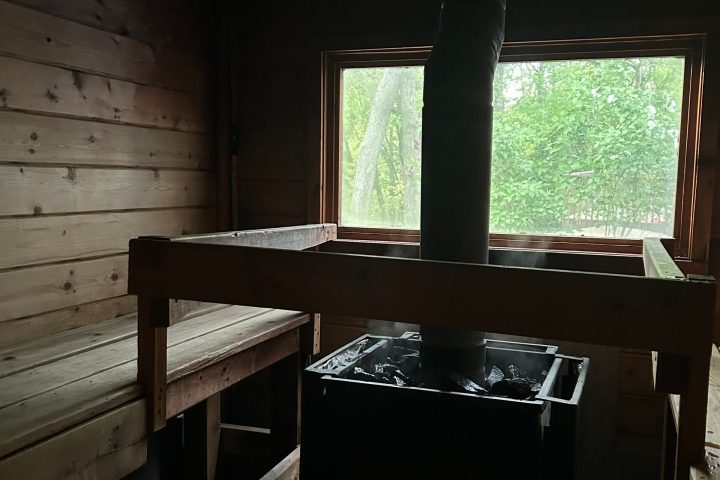 Interior of a wooden sauna with benches and a stove, window in the background.